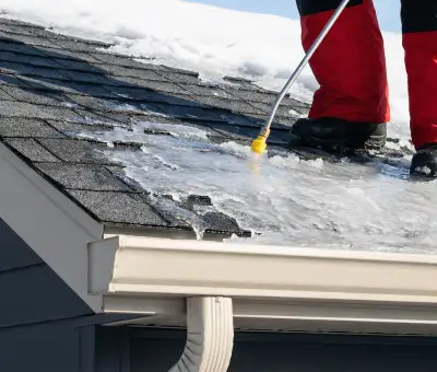 Ice dam removal technician using a steam wand to melt thick ice buildup on a residential roof in Cincinnati, OH