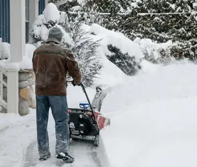Residential snow removal technician using a snow blower to clear a home driveway and walkway in Cincinnati, OH