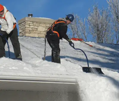 Professional technicians performing roof snow removal with safety harnesses and shovels in Cincinnati, OH